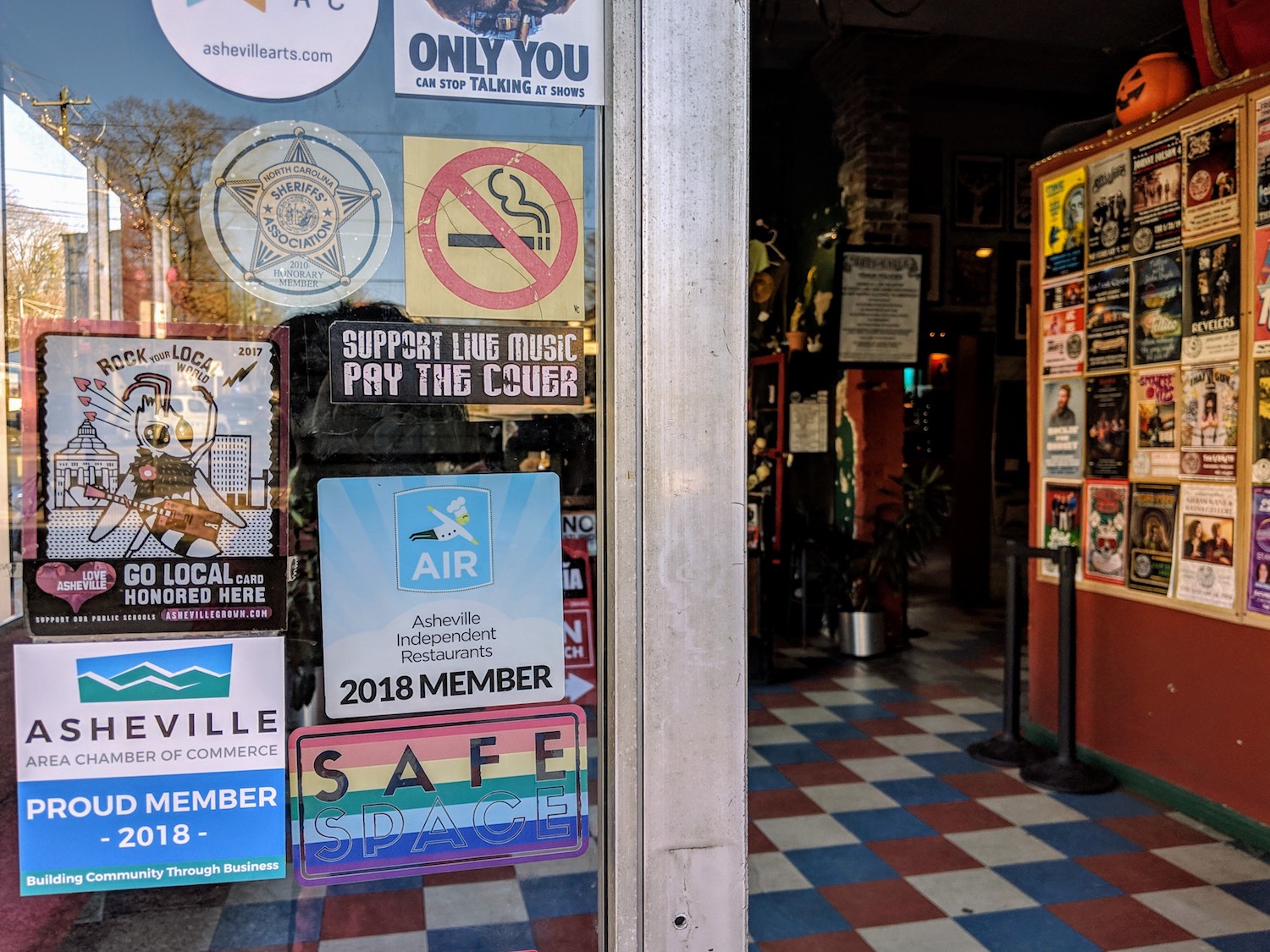 Doors to the Grey Eagle in Asheville with stickers on it that include No Smoking, an LGBTQ Safe Space and  proud member of the Asheville Area Chamber of Commerce.