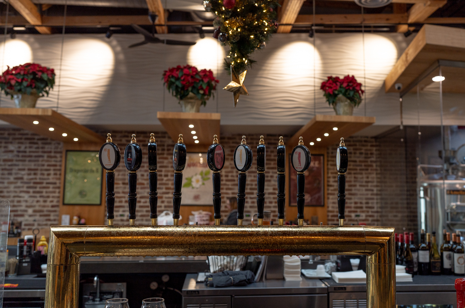 The inside of Amelia Island Brewing Company. The photo is centered on the tap handles for AIBC, which are black with gold trim. The background is blurred out and is brick and has a few poinsettas hanging from wooden planks that host round lights.