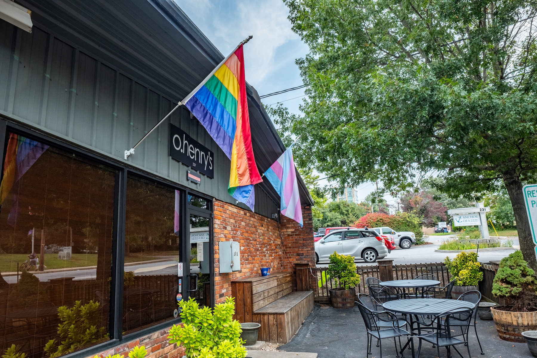 a photo of the outside patio of o.henry's in Asheville. There are two gay flags, one older version of the LGBTQ pride flag and another that represents the transgender community hanging from the building. 